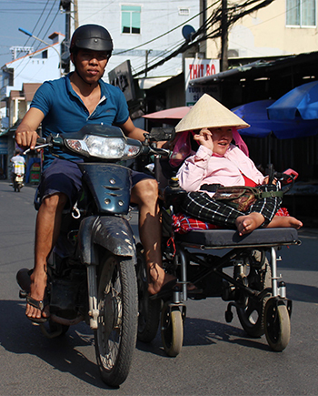 Anh Trí đi xe máy đẩy chiếc xe lăn của vợ về phòng trọ. Ảnh: Phan Diệp.